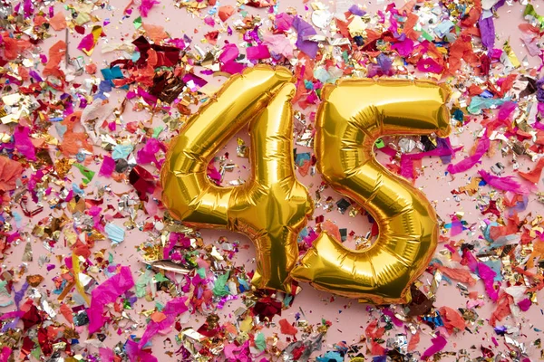 Number 45 gold birthday celebration balloon on a confetti glitter background