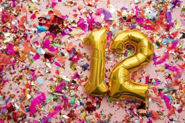 Number 12 gold birthday celebration balloon on a confetti glitter background