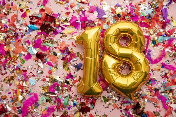 Number 18 gold birthday celebration balloon on a confetti glitter background — Stok fotoğraf