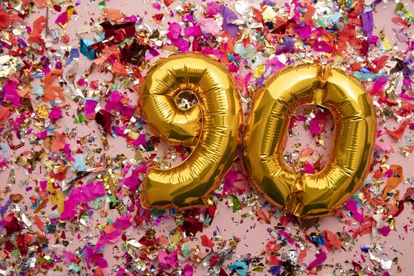 Number 90 gold birthday celebration balloon on a confetti glitter background