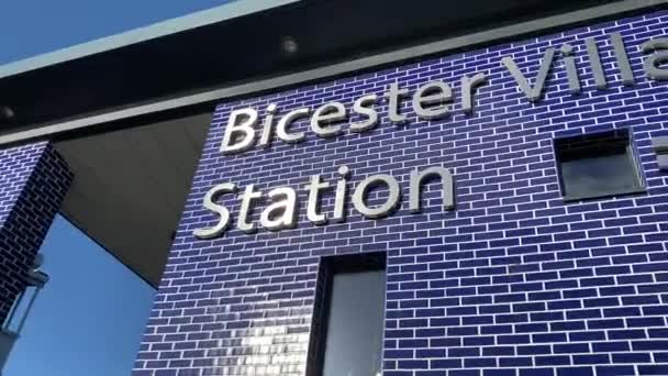 BICESTER, Reino Unido - 1 de marzo de 2020: Cámara panorámica a través de un cartel para la estación de tren Bicester Village en Oxfordshire — Vídeo de stock