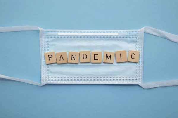 Mascarilla médica protectora con la palabra pandemia sobre un fondo azul — Foto de Stock