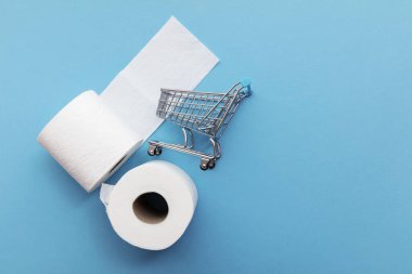 Mavi arka planda alışveriş arabası olan beyaz tuvalet kağıdı rulosu.