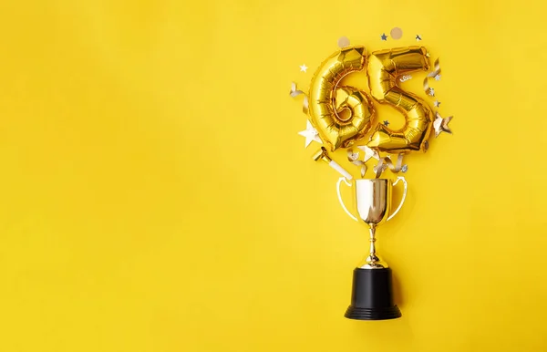 Number 65 gold anniversary celebration balloon exploding from a winning trophy — Stock Photo, Image