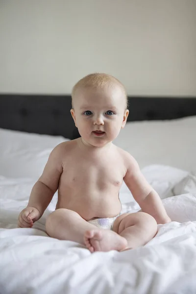 Bebê bonito usando uma fralda sentou-se em uma cama olhando para a câmera — Fotografia de Stock