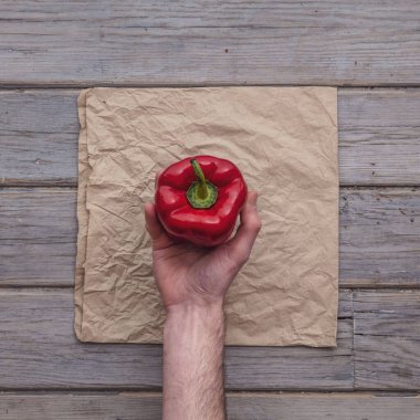Kırsal bir zemine karşı taze kırmızı biber tutan bir erkek el.