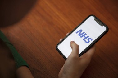 LONDON, İngiltere - 6 Nisan 2020: NHS sağlık hizmetleri akıllı telefon uygulaması kullanan bir kişi