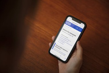 LONDON, İngiltere - 6 Nisan 2020: NHS sağlık hizmetleri akıllı telefon uygulaması kullanan bir kişi
