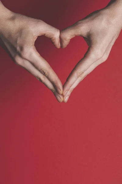 Vrouwelijke handen creëren de vorm van een liefde hart over een rode achtergrond. — Stockfoto