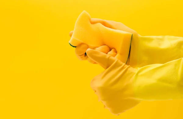 Mão usando uma luva de borracha amarela segurando uma esponja de limpeza — Fotografia de Stock