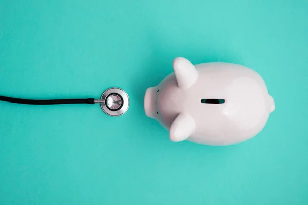 Náklady na zdravotní péči. Piggy bankovní pokladna s lékařskými lékaři stetoskop — Stock fotografie