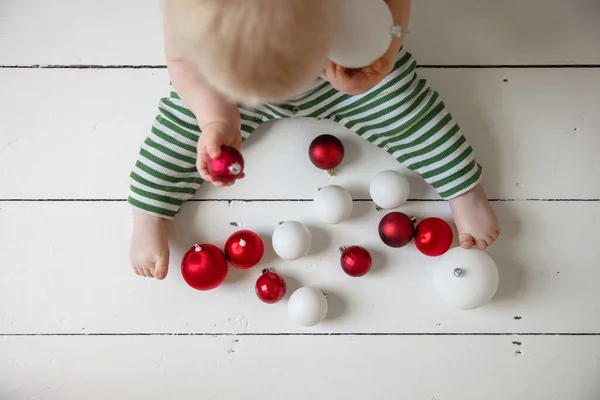 Bebê em uma roupa verde listrada brincando com bugigangas de Natal — Fotografia de Stock