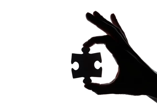 Silhouette d'une main tenant une pièce de puzzle sur fond blanc — Photo