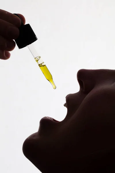 Silhouette of a woman taking drops of CDB oil — Stock Photo, Image