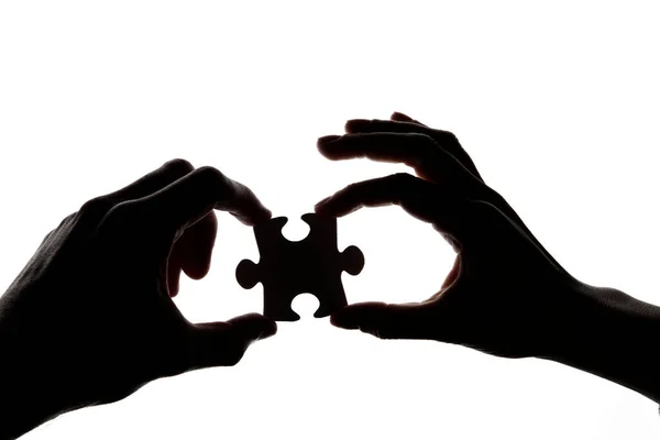 Silhueta de umas mãos que mantêm uma peça de quebra-cabeça de quebra-cabeça em um fundo branco — Fotografia de Stock