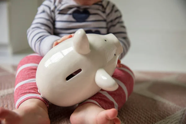 Náklady na koncepci péče o děti. Mladé dítě se drží bílé prasátko banky — Stock fotografie