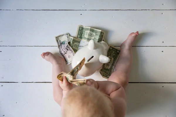 Mladé dítě sedí na podlaze a dává peníze do krabičky na peníze z prasátka — Stock fotografie