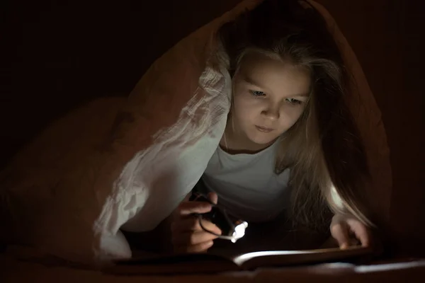 Little girl child read book in bed under the covers at night