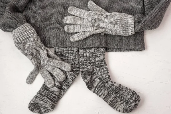 Warm female gray knitted gloves, scarf, socks on white textured background. Flat lay, top view minimal fashion concept.