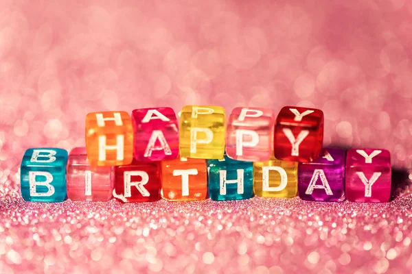 Happy Birthday with colored blocks letters on pink glitter backgrounds. Postcard to celebrate.