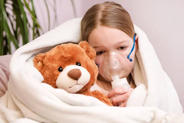 Respiratory inhalation, personal care, hospital. Kid girl, asthma problem. Little girl Sitting with a toy on the couch in a mask for inhalations, making inhalation with nebulizer at home inhaler.