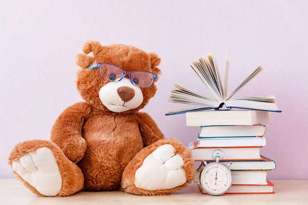 Soft stuffed toy Teddy bear with glasses, a stack of books and a stopwatch. Education concept, back to school, reading speed