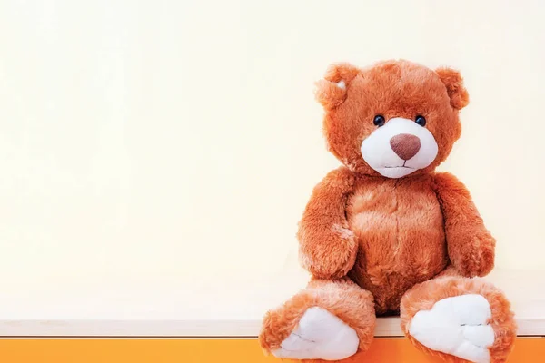 Teddy Bear stuffed toy sits on shelf on yellow background. Education, parenting and childhood baby concept. Copy space for text.
