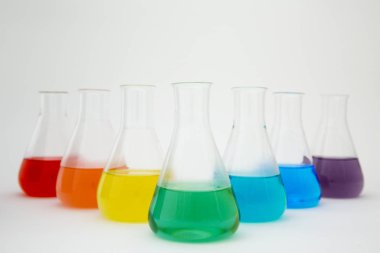 Beyaz arka planda gökkuşağı oluşturan renkli sıvılarla dolu bilimsel laboratuar camı Erlenmeyer şişesi..