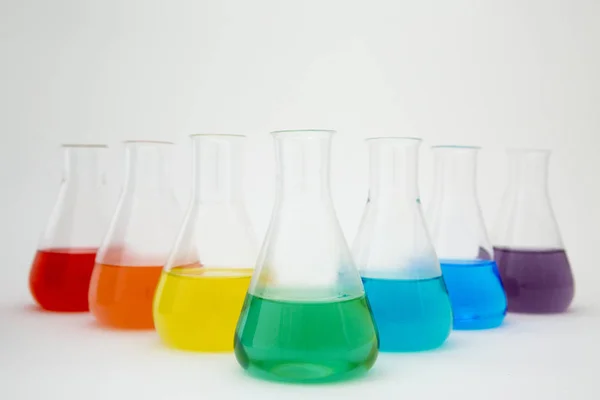 Frasco erlenmeyer de vidrio de laboratorio científico lleno de líquido colorido que forma el arco iris sobre fondo blanco. — Foto de Stock