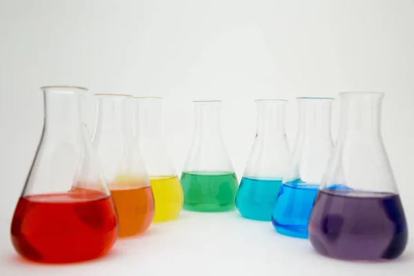 Frasco erlenmeyer de vidrio de laboratorio científico lleno de líquido colorido que forma el arco iris sobre fondo blanco. — Foto de Stock