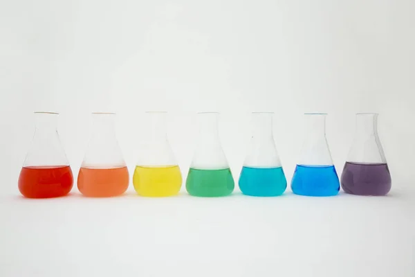 Vědecké laboratorní sklo erlenmeyer baňka naplněná barevnou kapalinou tvářecí duha na bílém pozadí. — Stock fotografie