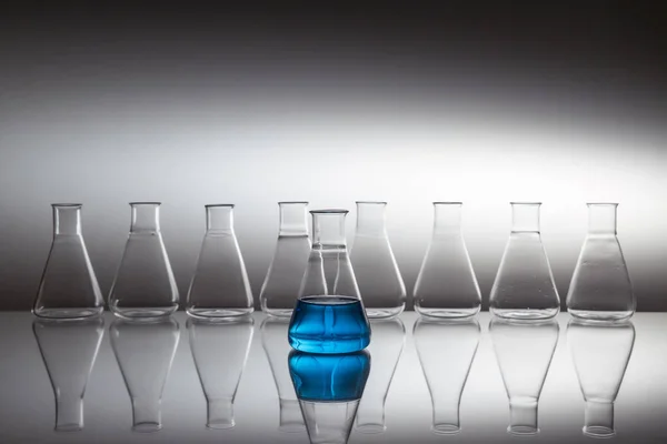 反射面にガラス器具で満たされた青色の液体で満たされた科学実験室のガラスエルレンマイヤーフラスコ. — ストック写真