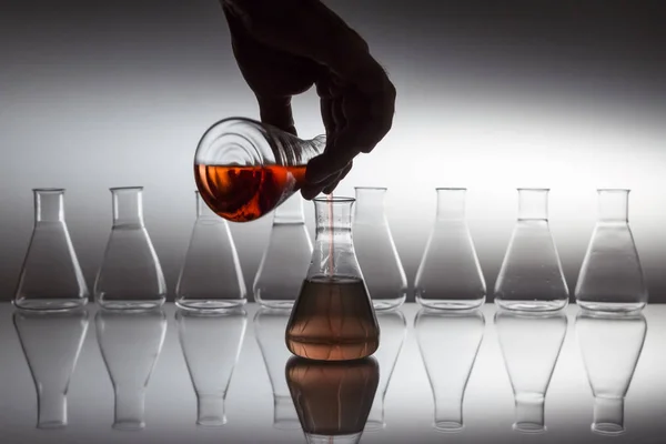 反射面にガラス器具を備えた科学実験室用ガラスエルレンマイヤーフラスコに液体を注ぐ手. — ストック写真