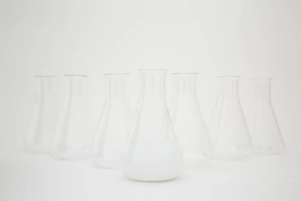 Bilimsel laboratuvar camı Erlenmeyer şişesi beyaz arka planda cam ekipmanla dolu beyaz sıvı dolu.. — Stok fotoğraf
