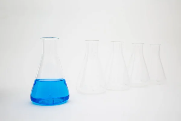 Frasco de vidro erlenmeyer de laboratório científico cheio de líquido azul com equipamento de vidro sobre fundo branco . — Fotografia de Stock