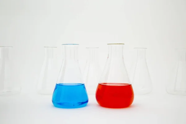 Laboratorní laboratorní skleněná Erlenmeyerova baňka naplněná modrou a červenou tekutinou se skleněným zařízením na bílém pozadí. — Stock fotografie
