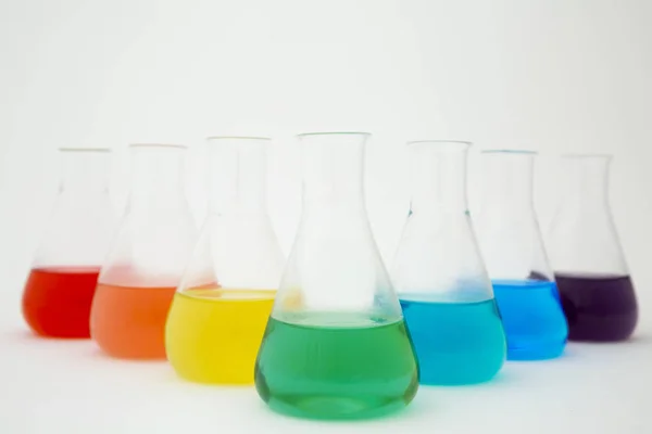 Frasco de erlenmeyer de vidro de laboratório científico preenchido com líquido colorido formando arco-íris no fundo branco. — Fotografia de Stock