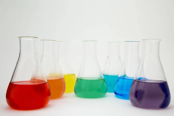 Frasco erlenmeyer de vidrio de laboratorio científico lleno de líquido colorido que forma el arco iris sobre fondo blanco. — Foto de Stock