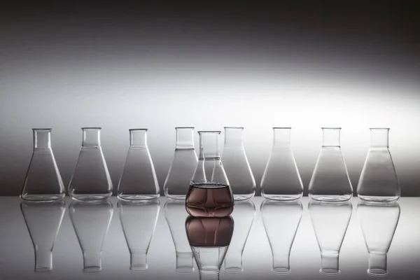 Bilimsel laboratuvar camı Erlenmeyer şişesi yansıtıcı yüzeyde cam ekipmanlarla dolu mor sıvıyla dolu.. — Stok fotoğraf