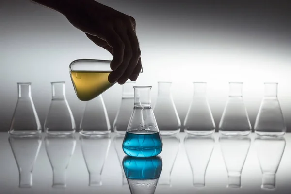 분광기 표면에 유리 제품이 달린 유리에 렌메어 플라스크를 과학 실험실에 있는 푸른 액체에 노란색으로 붓는 모습. — 스톡 사진