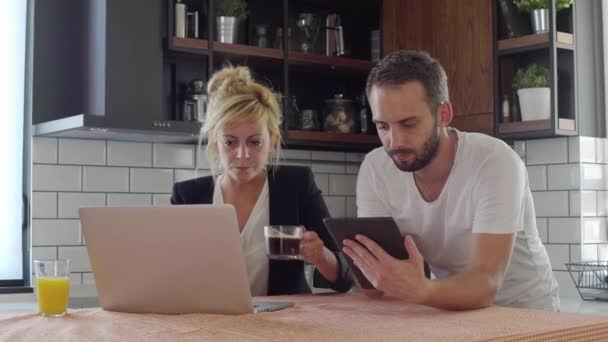 夫妻二人在厨房喝咖啡休息的时候上网搜寻 他们正在研发平板电脑和笔记本电脑 — 图库视频影像
