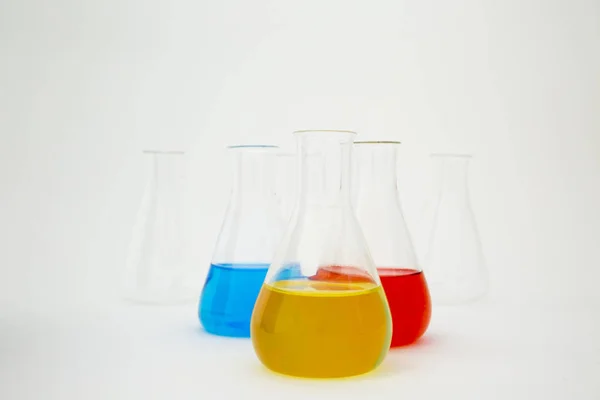 Scientific laboratory glass erlenmeyer flask filled with blue, yellow and red liquid on white background. — Stock Photo, Image