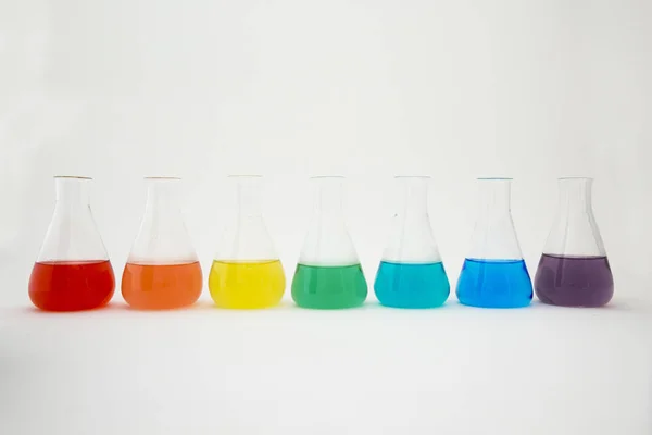 Laboratorium naukowe szkło erlenmeyer kolba wypełniona kolorowy płyn tworzący tęczę na białym tle. — Zdjęcie stockowe