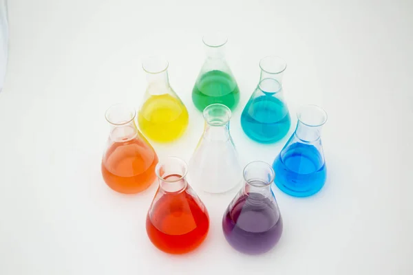 Beyaz arka planda gökkuşağı oluşturan renkli sıvılarla dolu bilimsel laboratuar camı Erlenmeyer şişesi.. — Stok fotoğraf