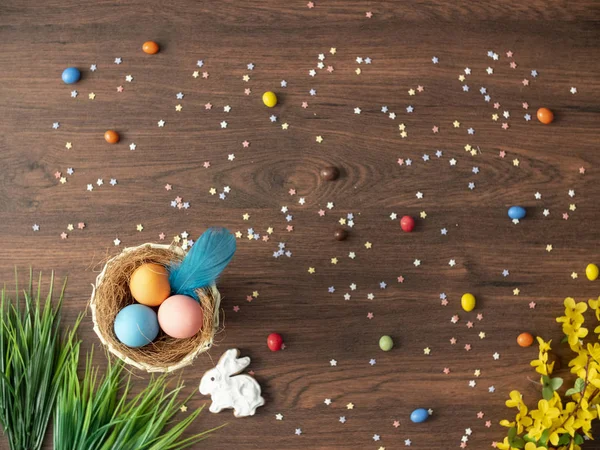 Bunte Ostereier im Nest, Frühlingsblumen und Bonbons auf dem Holztisch. Osterfestdekoration, Osterkonzept Hintergrund. — Stockfoto