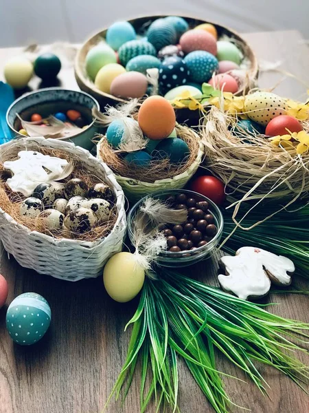 Színes húsvéti tojások fészekben, tollak és tavaszi virágok a fa asztalon. Húsvéti ünnepi dekorációk, húsvéti koncepció háttér. — Stock Fotó