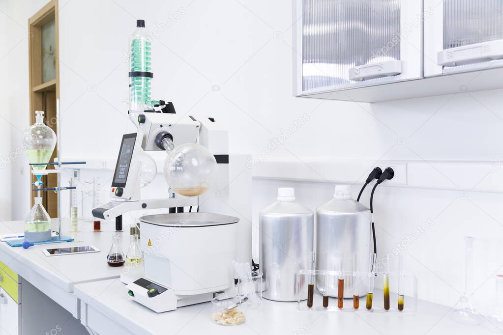 Rotational vaporizer called rotavapor with green condenser placed on desk in modern laboratory. CBD extracts are on table in erlenmeyer flasks. Cannabis pharmaceutical healthcare process.