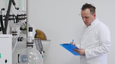 Bilim adamı CBD yağ çıkarma sırasında laboratuvarda rotovapor inceliyor. Lastik eldiven takıyor ve yeşil yoğunlaştırıcılı döner buharlaştırıcının yanında duruyor.. 