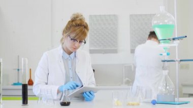 Laboratuvarda kenevir CBD, CBDA yağları ve tabletle çalışan iki bilim adamı. Lateks eldiven, cam tüpler ve erlenmeyer şişeleri kullanıyorlar. Esrar tohumlarından alınan sağlık hizmetleri eczanesi.