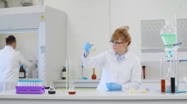 Laboratuvarda kenevir CBD, CBDA yağları ve tabletle çalışan iki bilim adamı. Lateks eldiven, cam tüpler ve erlenmeyer şişeleri kullanıyorlar. Esrar tohumlarından alınan sağlık hizmetleri eczanesi.